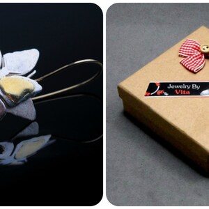 May include: Silver and gold butterfly earrings with a delicate chain detail. The earrings are packaged in a brown box with a red and white gingham bow and a "Jewelry By Vita" label.