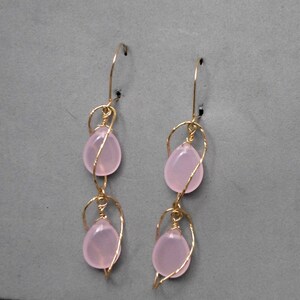 May include: A pair of gold wire earrings with two pink teardrop-shaped stones on each earring.