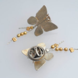 May include: Two silver butterfly brooches with gold bead chains. Each brooch has a pin back.