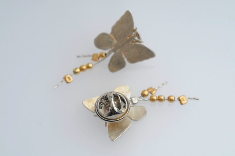 May include: Two silver butterfly brooches with gold bead chains. Each brooch has a pin back.