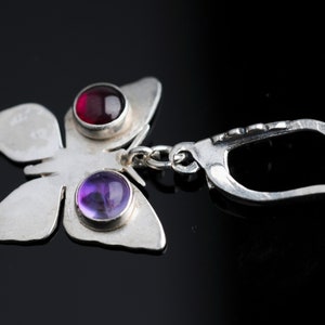 May include: Silver butterfly earring with a red and purple gemstone. The earring has a lever back closure.