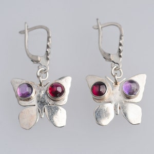May include: Silver butterfly earrings with purple and red gemstone accents.