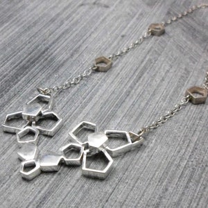 May include: A silver necklace with a geometric pendant made of interconnected hexagonal shapes. The pendant is attached to a delicate silver chain.