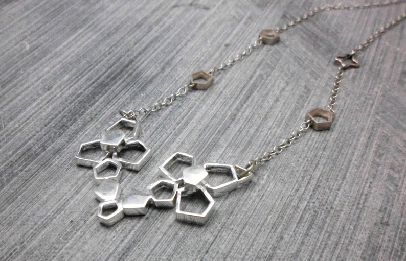 May include: A silver necklace with a geometric pendant made of interconnected hexagonal shapes. The pendant is attached to a delicate silver chain.