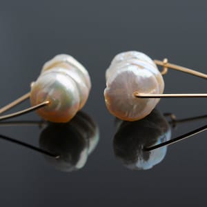 May include: A pair of gold earrings with a large, white, baroque pearl on each earring.