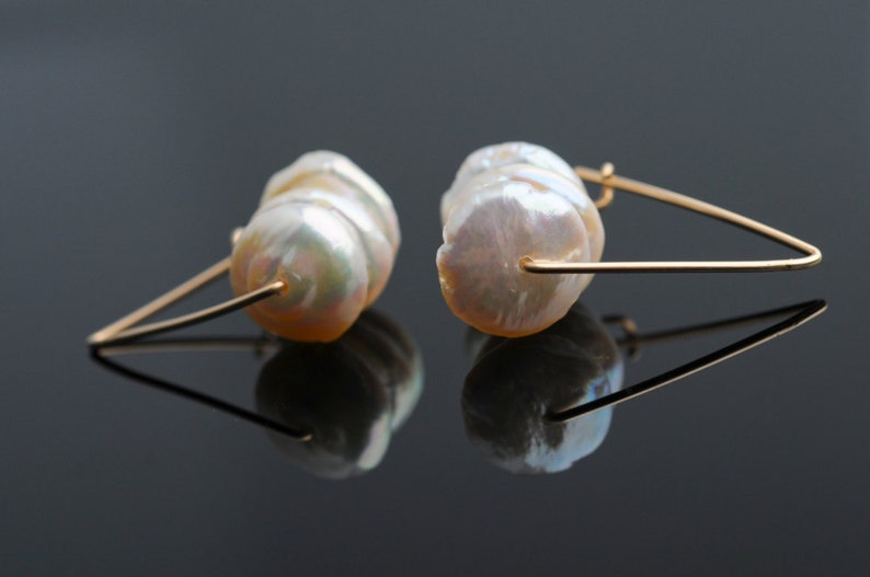 May include: A pair of gold earrings with a large, white, baroque pearl on each earring.