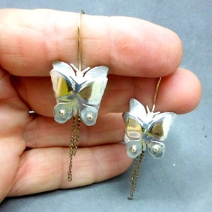 May include: A pair of silver butterfly earrings with gold accents and dangling chains.