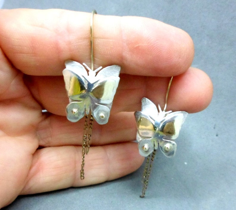May include: A pair of silver butterfly earrings with gold accents and dangling chains.
