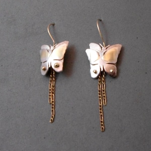May include: A pair of silver butterfly earrings with gold accents and dangling gold chains.