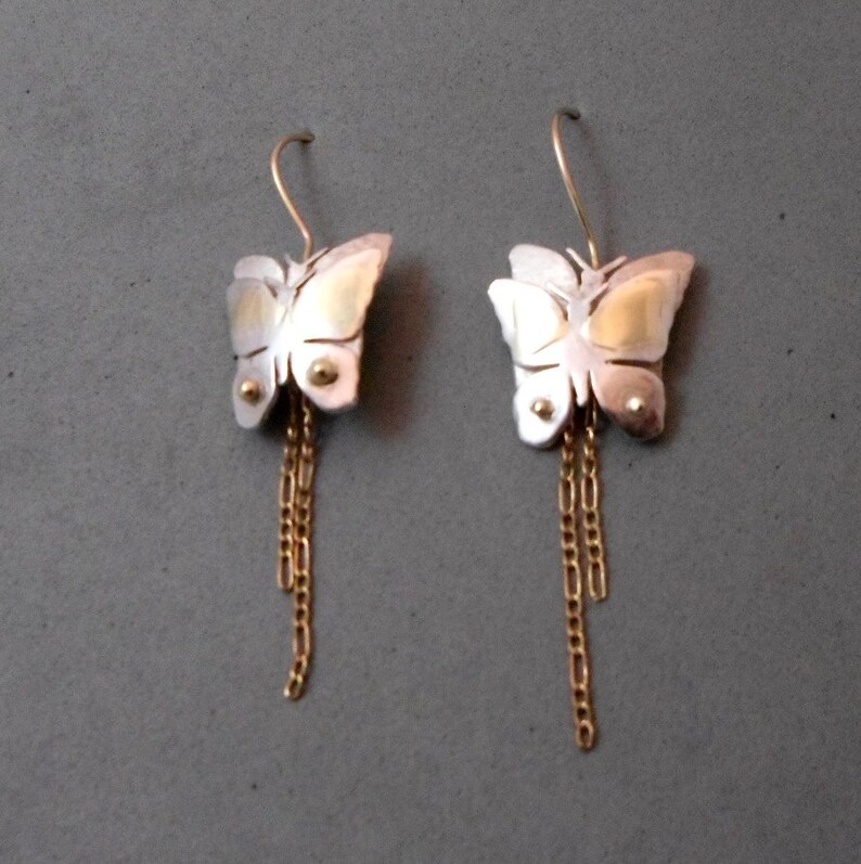 May include: A pair of silver butterfly earrings with gold accents and dangling gold chains.
