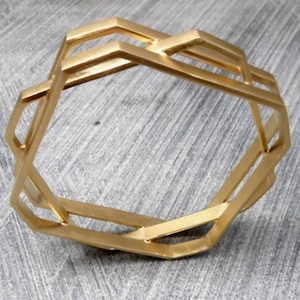 May include: A gold-colored geometric bracelet with an open design. The bracelet features a series of interconnected, angular shapes, creating a modern and stylish accessory. The bracelet is made of metal and has a matte finish.