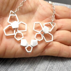 May include: A silver necklace with a geometric pendant made of interconnected shapes. The pendant is in the shape of a flower with multiple layers.