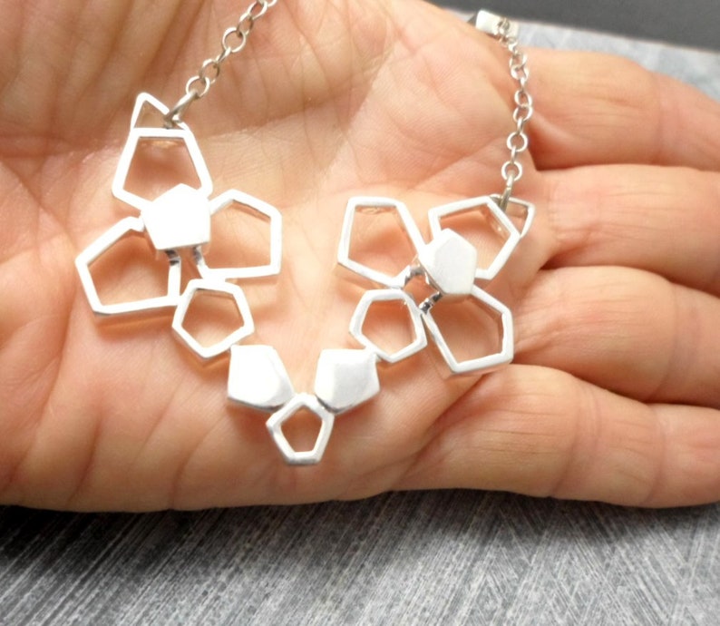 May include: A silver necklace with a geometric pendant made of interconnected shapes. The pendant is in the shape of a flower with multiple layers.