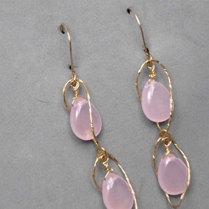 May include: A pair of gold earrings with two pink teardrop-shaped stones on each earring. The stones are suspended from a delicate gold wire design.