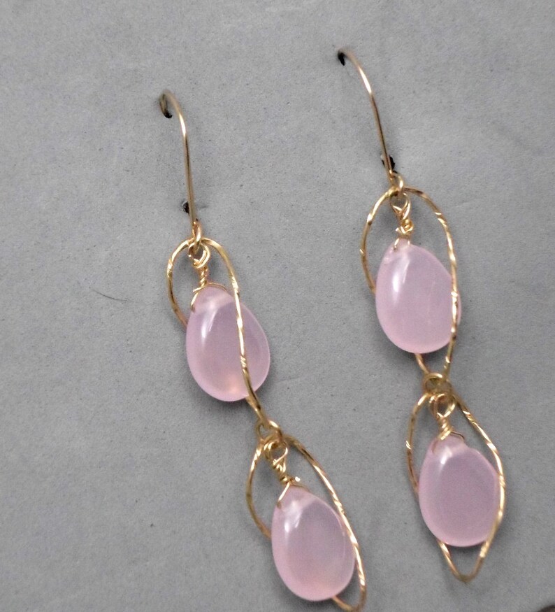 May include: A pair of gold earrings with two pink teardrop-shaped stones on each earring. The stones are suspended from a delicate gold wire design.