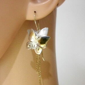 May include: Silver and gold butterfly earrings with a chain dangle. The butterfly is textured and has a three-dimensional design.