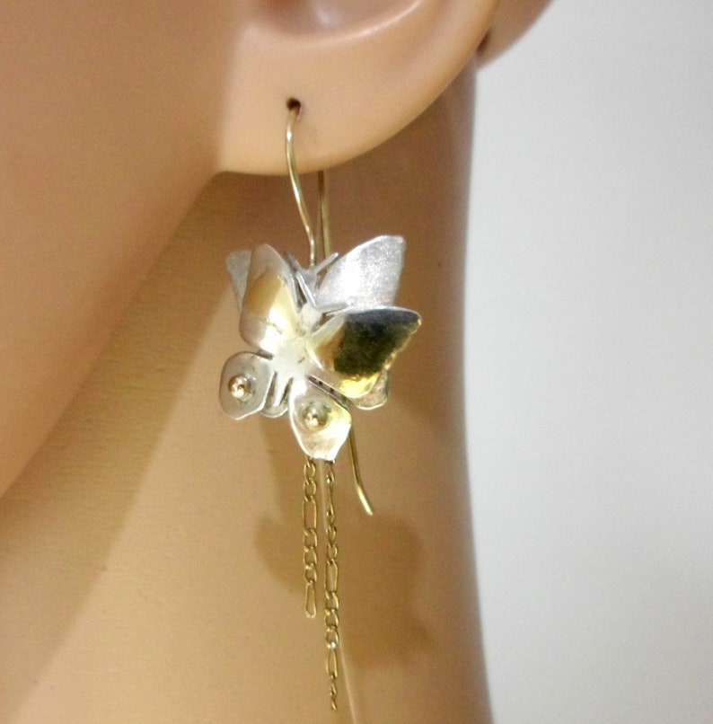 May include: Silver and gold butterfly earrings with a chain dangle. The butterfly is textured and has a three-dimensional design.