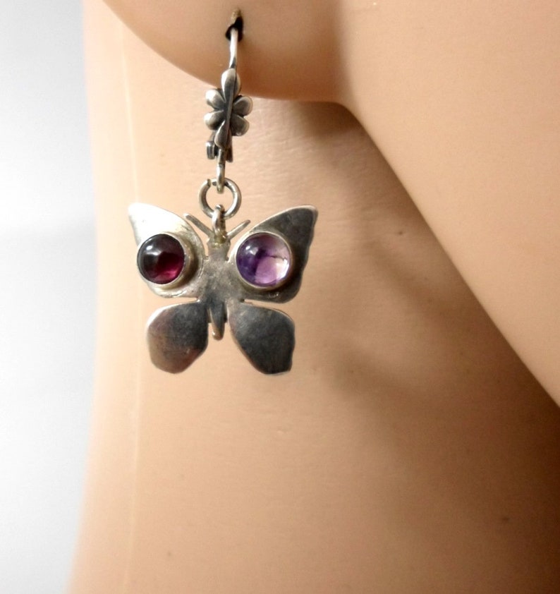 May include: Silver butterfly earrings with purple and red gemstone accents.
