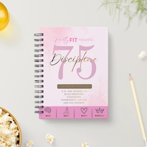 Könnte beinhalten: Ein spiralgebundenes Notizbuch mit hellrosa Einband und dem Text Pretty FIT PRESENTS 75 Discipline, #THEDISCIPLINEDIARIES, A 75-DAY JOURNEY TO BUILD DISCIPLINE, CONFIDENCE, CONSISTENCY, AND THE LIFE YOU DESERVE, sowie Icons für MIND, BODY, SPIRIT, PURPOSE.