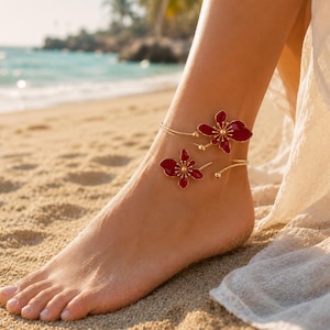 May include: A gold-toned metal anklet featuring two open-ended wire bands, each adorned with a deep red enamel flower motif. The floral elements have gold-colored centers and delicate petals, creating a layered appearance around the ankle.
