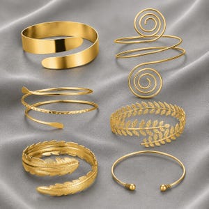 May include: A collection of six gold-toned metal arm cuffs and bracelets. The set includes a smooth wide band, a double spiral wire cuff, a textured spiral wire cuff, a leaf-patterned band, a feather-shaped wrap bracelet, and a thin wire cuff.
