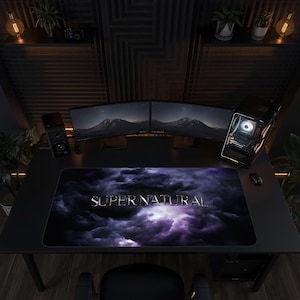 Può includere: Un tappetino da scrivania rettangolare con un design a nuvole scure viola e nere e la parola SUPERNATURAL stampata in un carattere metallico color argento al centro, posizionato su una superficie di una scrivania nera.