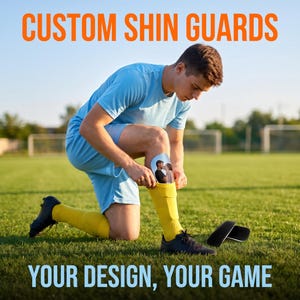 Könnte beinhalten: Individuelle Schienbeinschoner mit einem personalisierten Foto eines Paares. Die Schienbeinschoner sind weiß, gebogen geformt und werden unter gelben Socken getragen. Der Text CUSTOM SHIN GUARDS und YOUR DESIGN, YOUR GAME ist abgebildet.