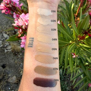 May include: A series of eight skin tone cosmetic swatches applied in a vertical line on an arm, labeled 01N through 08N. The shades range from a light beige at the top to a deep dark brown at the bottom, showing a gradient of neutral foundation colors.