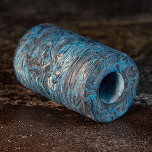 May include: A cylindrical object featuring a marbled pattern of deep blue, black, and metallic copper swirls. The item has a smooth, polished finish and a circular opening at one end, showcasing a continuous, fluid design across its entire surface.