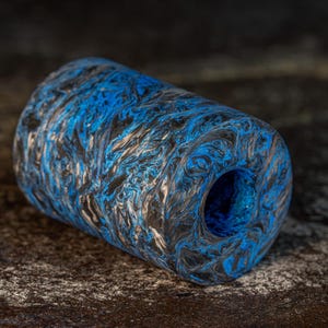 May include: A cylindrical object featuring a marbled pattern of vibrant blue, black, and white swirls. The item has a hollow center, creating a tube-like structure with a smooth, polished finish that highlights the intricate, flowing color transitions.