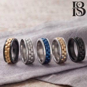 May include: Five rings arranged in a row, each featuring a central band designed to resemble a watch link bracelet. The rings are finished in various colors including gold and black, silver, blue, silver and gold, and solid black.