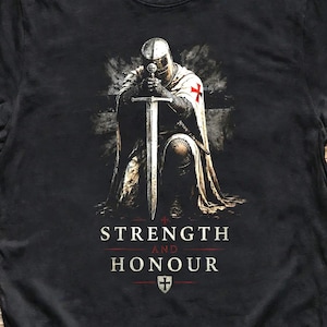 May include: A black short-sleeved t-shirt featuring a graphic of a knight kneeling with a sword. The knight wears a white cloak with a red cross. Below the graphic, the text reads STRENGTH AND HONOUR with a small shield icon containing a cross.