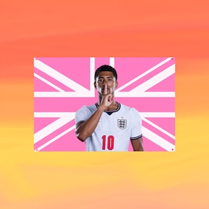 May include: A rectangular wall banner featuring a portrait of a football player wearing a white jersey with the number 10 and a team crest. The player has a finger held to their lips in a shushing gesture. The background is a pink Union Jack flag.