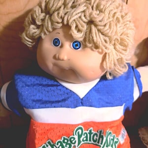 Muñeco Cabbage Patch Kids vintage de 1985: niño de ojos azules con cabello rubio de lana, uniforme deportivo original y pañal, firmado por Xavier Roberts '85.