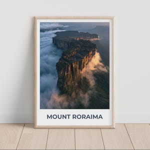 Può includere: Una stampa artistica incorniciata che mostra una vista aerea del Monte Roraima, una montagna dalla cima piatta circondata da dense nuvole bianche. La parete rocciosa è illuminata da una calda luce dorata, con il testo MOUNT RORAIMA stampato sotto.