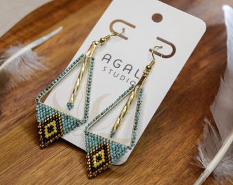 Pode incluir: Um par de brincos pendentes num cartão expositor branco com a etiqueta AGAL STUDIO. Os brincos apresentam uma estrutura triangular dourada com uma barra central dourada e uma secção de missangas em azul claro, amarelo e preto.
