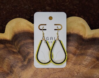 Pode incluir: Um par de brincos em forma de gota com uma armação de metal dourado decorada com missangas alternadas em preto e amarelo brilhante. Os brincos estão fixados num cartão branco com o texto GAL STUDIO impresso a preto.