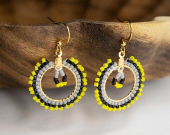 May include: A pair of dangle earrings featuring circular gold-tone metal frames adorned with small, square-shaped beads in alternating patterns of bright yellow, black, and light gray. Each earring includes a gold-tone hook and a small central loop.