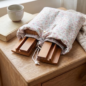 May include: A floral print fabric drawstring pouch in white with small pink and blue flowers, partially containing two rectangular wooden stands with grooved surfaces. The pouch features a white cord closure with small metallic end caps.