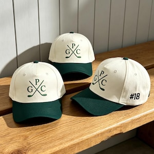May include: Three baseball caps with off-white crowns and dark green brims. Each cap features a dark green embroidered logo of two crossed golf clubs with the letters G, P, and C. One cap displays the number #18 in black on the side panel.