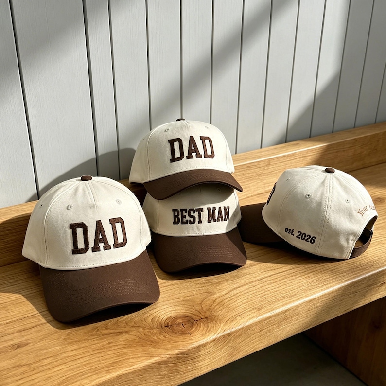 Puede incluir: Tres gorras de b&eacute;isbol con coronas color crema y viseras marr&oacute;n oscuro. Dos gorras presentan la palabra DAD en letras de bloque marr&oacute;n oscuro, una presenta BEST MAN, y un lado muestra el texto est. 2026 y Your text en bordado marr&oacute;n.