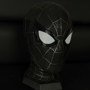 May include: A black full-head mask featuring a textured honeycomb pattern across the surface, a raised web design, and two large, almond-shaped white mesh eye lenses framed by glossy black borders, mounted on a black hexagonal display stand.