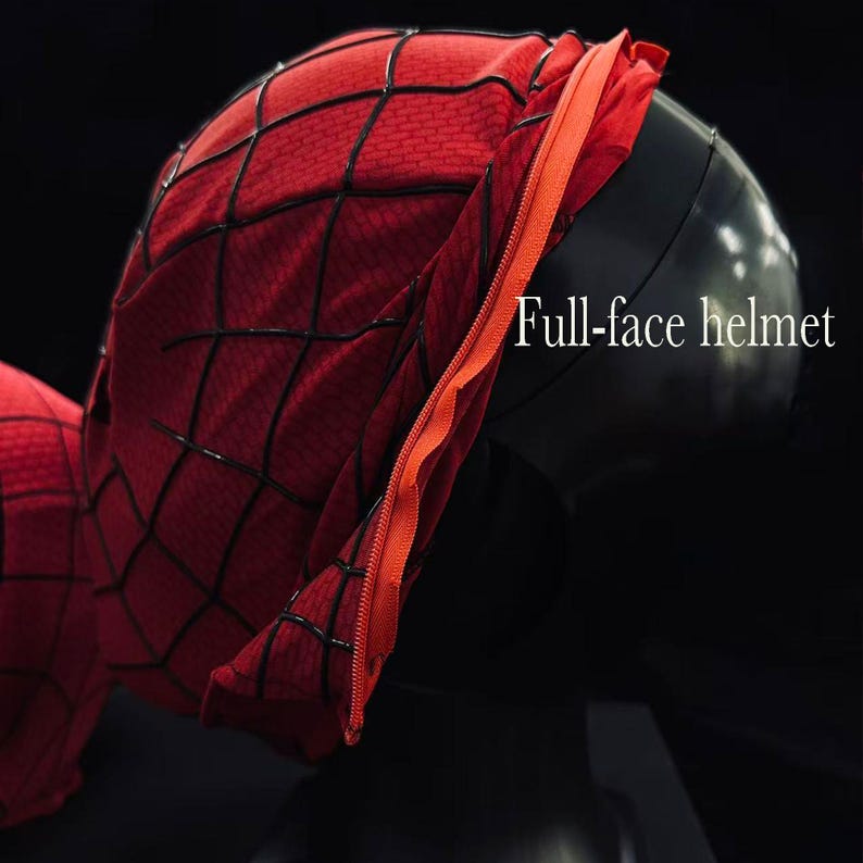 Puede incluir: Una m&aacute;scara de tela roja con un patr&oacute;n de telara&ntilde;a negra y una cremallera naranja en el lateral, expuesta sobre una cabeza de maniqu&iacute; negra. El texto Full-face helmet es visible en el lado derecho de la imagen sobre el fondo oscuro.