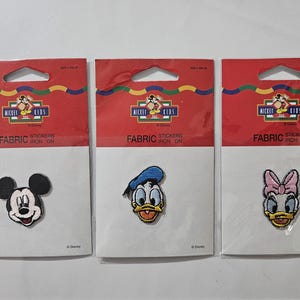 Könnte beinhalten: Drei einzelne Packungen mit Disney Mickey Kids Stoff-Aufbügelstickern. Jede Packung enthält einen Charakter-Aufnäher: Mickey Maus, Donald Duck und Daisy Duck. Die Verpackung ist rot-weiß mit dem Mickey Kids Logo und Disney-Schriftzug.
