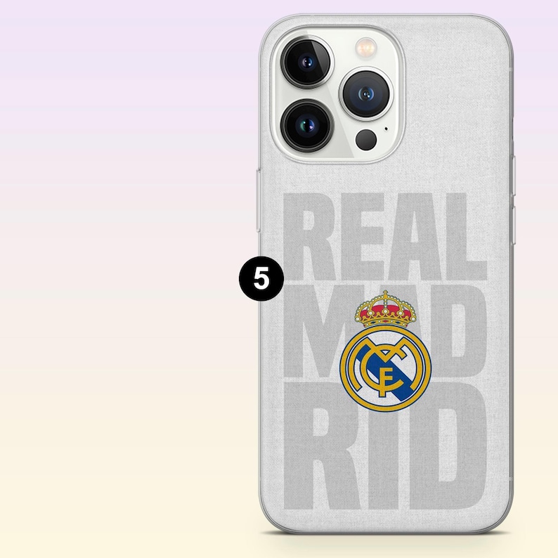 May include: A light gray smartphone case featuring the text REAL MADRID in large, bold, light gray letters. The official Real Madrid club crest, which includes a gold crown, a blue and gold circular emblem, and a red stripe, is centered on the case.