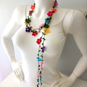 May include: A long, colorful crocheted necklace with small flower-shaped beads. The necklace is made of multiple strands of green yarn with colorful flowers in shades of red, orange, yellow, green, blue, purple, and pink.