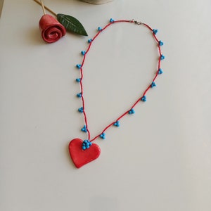 May include: A red heart-shaped pendant necklace with blue beads on a red string.