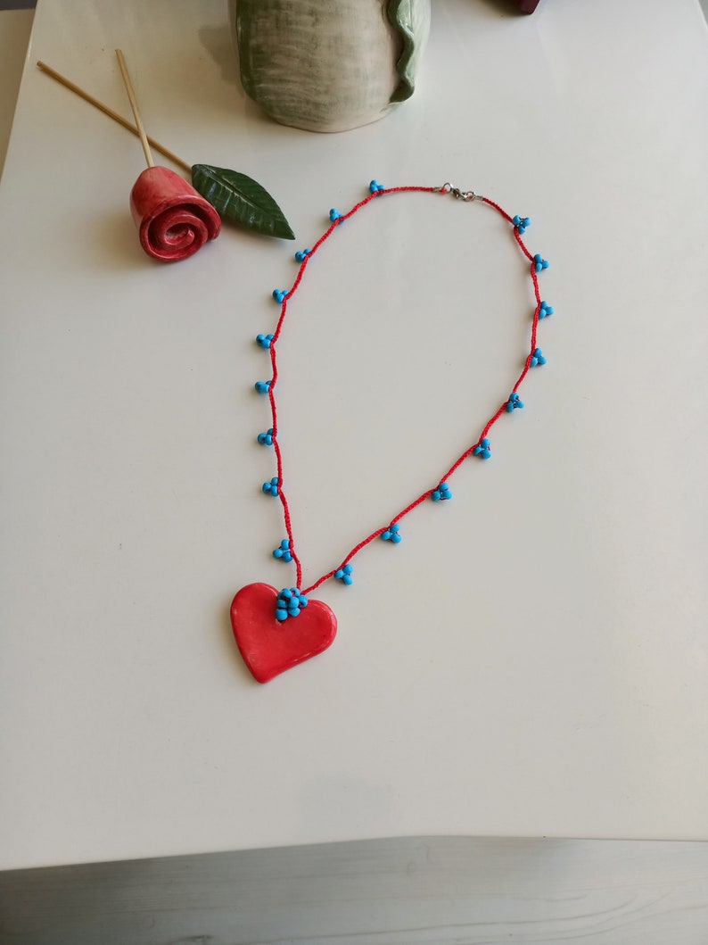 May include: A red heart-shaped pendant necklace with blue beads on a red string.