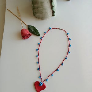 May include: A red heart pendant necklace with blue beads on a red cord.