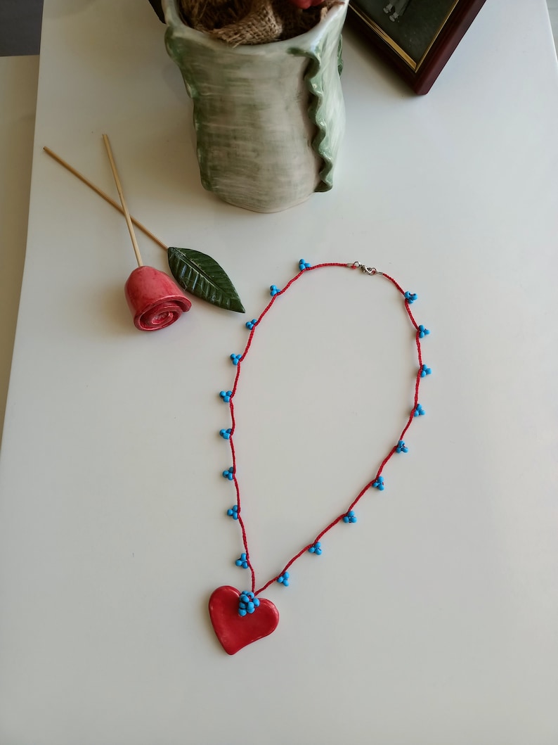 May include: A red heart pendant necklace with blue beads on a red cord.